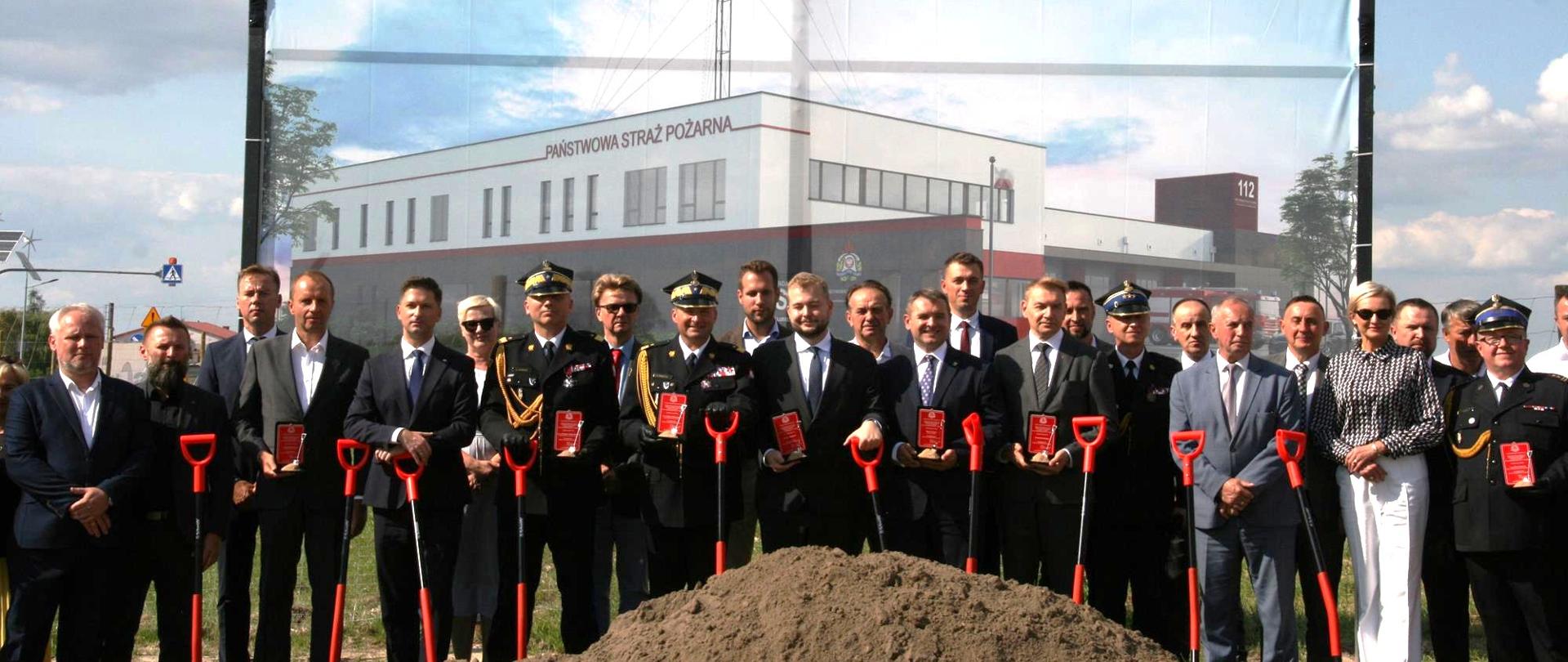 Grupa osób stoi trzymając łopaty w dłoniach, za nimi wizualizacja nowej komendy