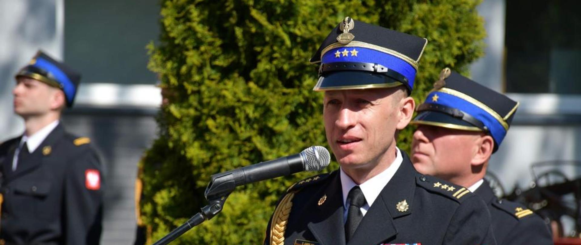 strażak przed mikrofonem, w tle zielone drzewa 