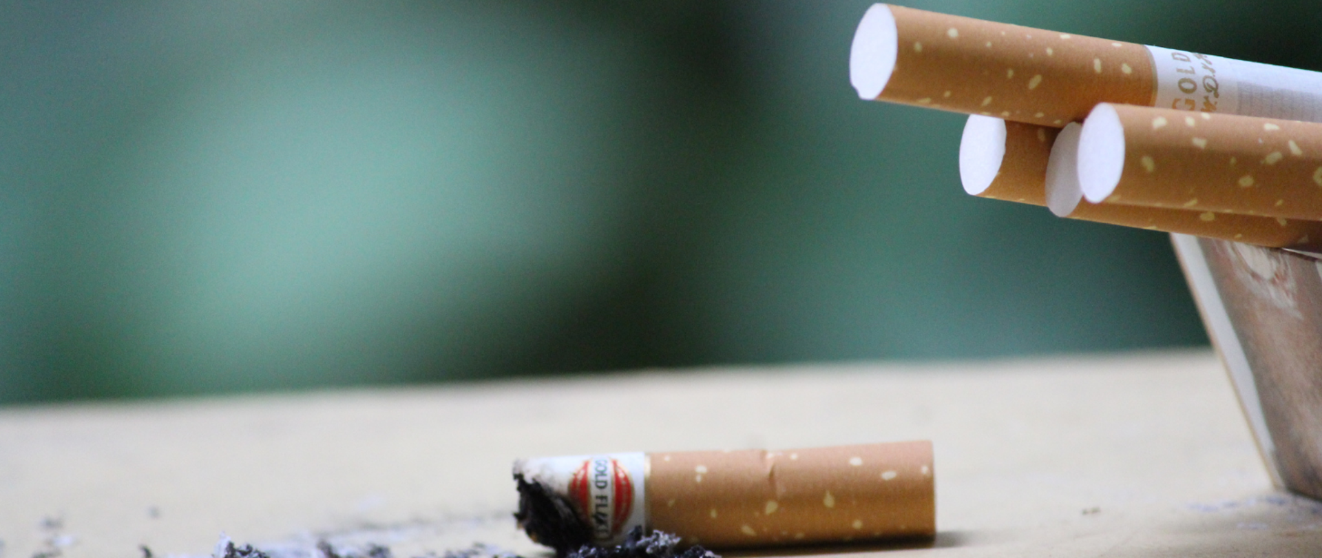 Kilka papierosów umieszczonych w popielniczce i jeden wypalony papieros oraz popiół leżące na stole
