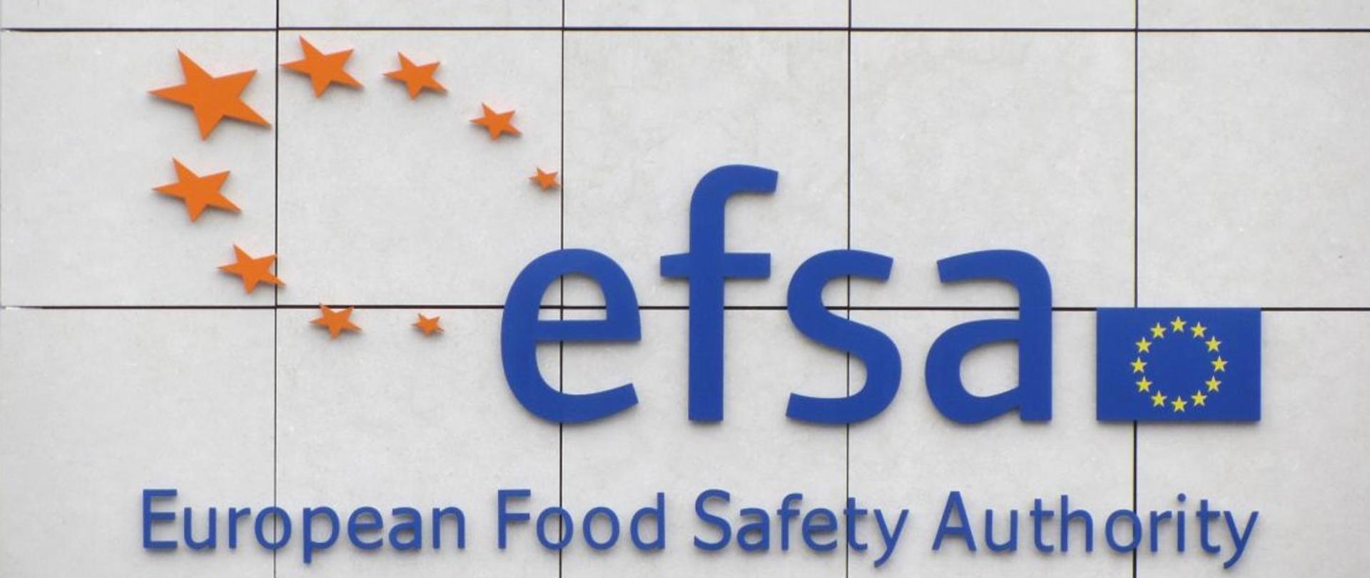 Na zdjęciu znajduje się flaga Unii Europejskiej, obok skrót EFSA oraz 9 gwiazdek ułożonych w owal. Pod skrótem napis - European Food Safety Authority.