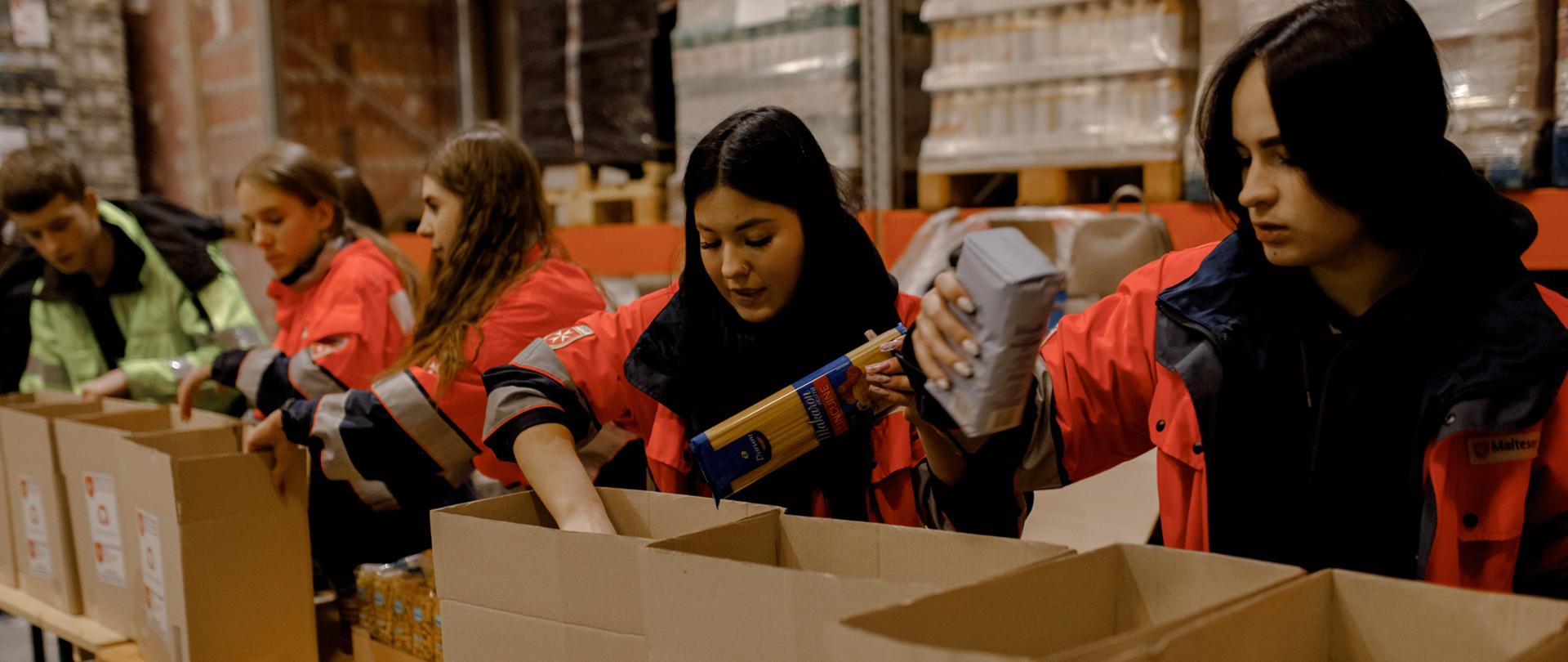 Na zdjęciu widać wolontariuszy znajdujących się w magazynie. Młodzież pakuje paczki żywnościowe dla potrzebujących. 
