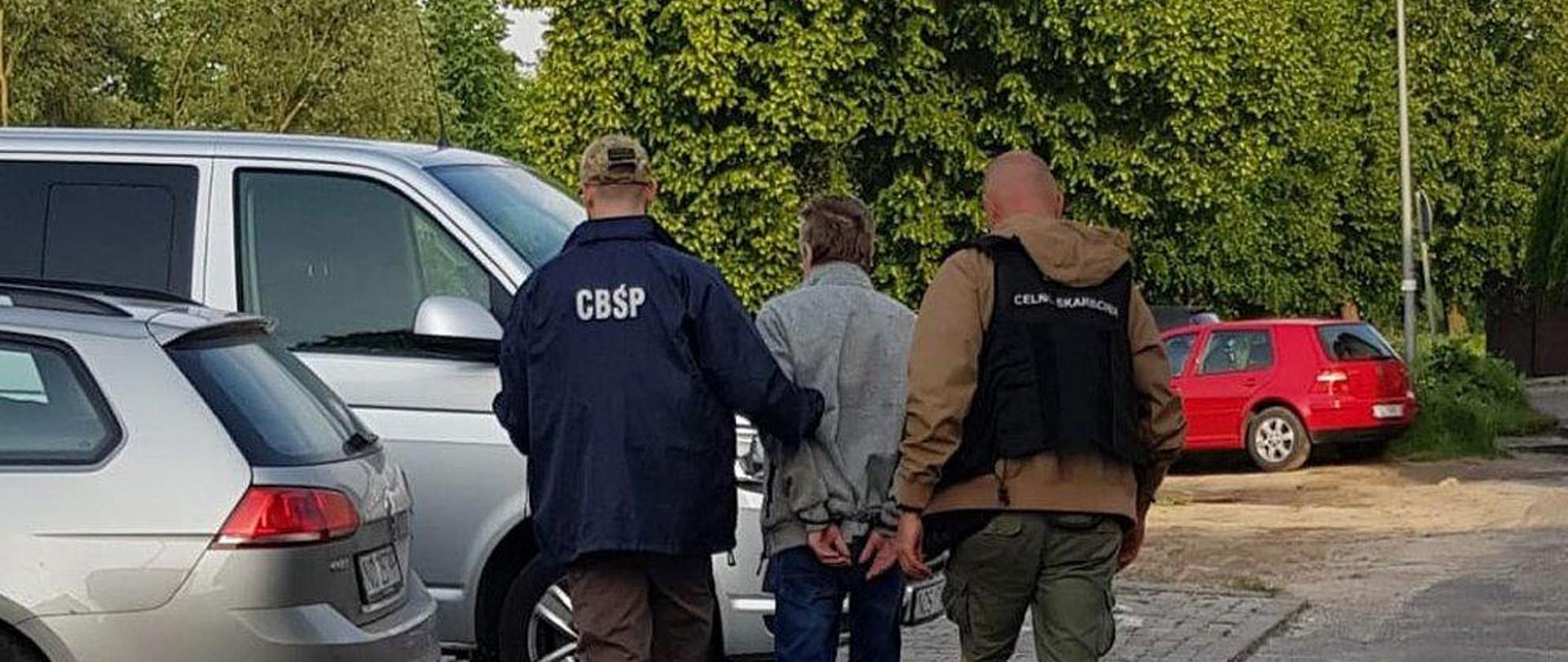 Funkcjonariusze CBŚP i Służby Celno-Skrabowej prowadzą skutego mężczyznę.