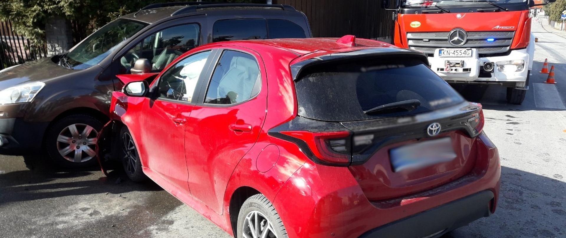 Czerwony samochód osobowy uderzył w bok samochodu ciemnego koloru.