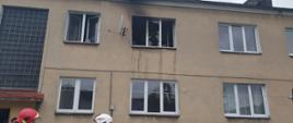Zdjęcie przedstawia ścianę budynku oraz wybite okno mieszkania objętego pożarem.