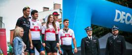 Na podium 5 zawodników w tym 1 kobieta w czarnych getrach i biało czerwonych koszulkach z znakiem orła, po prawej stronie stoi dwóch funkcjonariuszy PSP, po lewo kobieta 