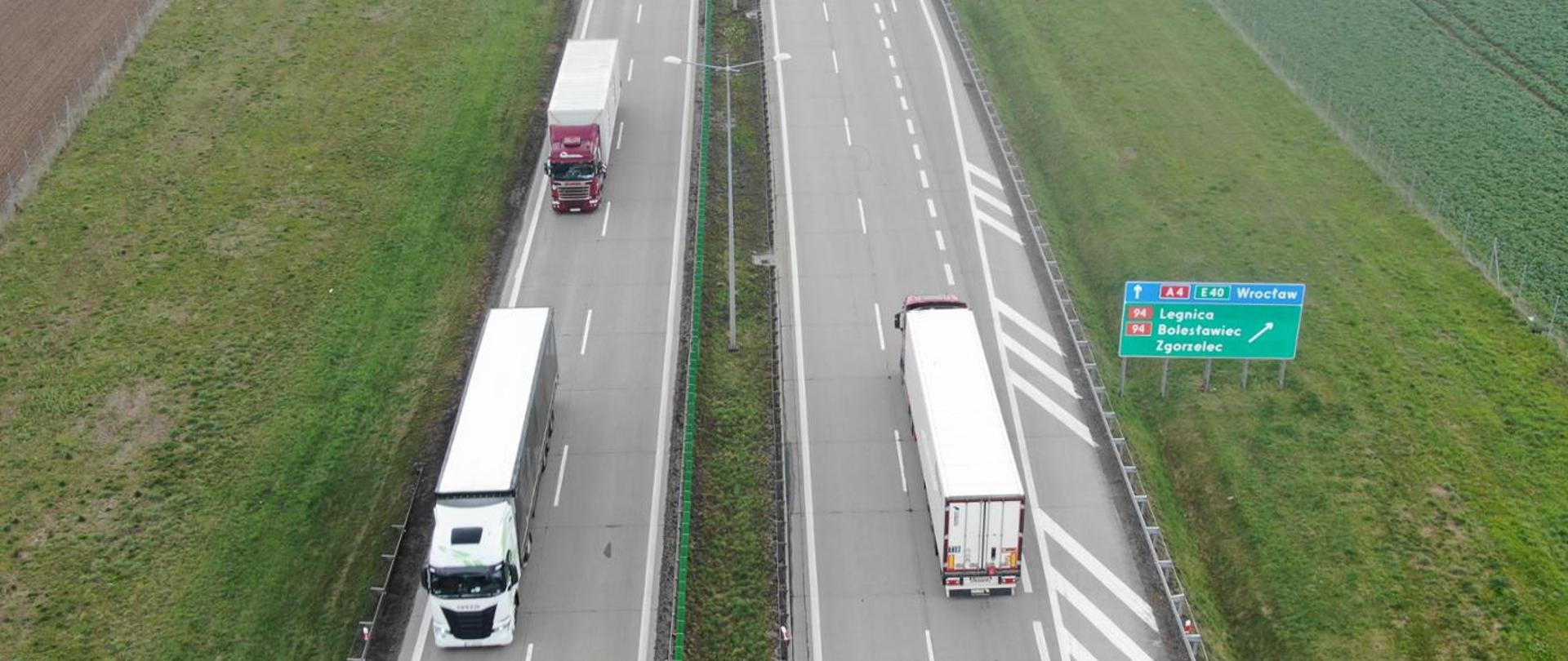 Autostrada A4 widziana z lotu ptaka, dwie jezdnie rozdzielone pasem zieleni. Po obu kierunkach jadą samochody ciężarowe. Po prawej stronie widoczna tablica drogowa z oznaczeniami: A4 E40 oraz kierunkami Wrocław, Legnica, Bolesławiec, Zgorzelec przy zjeździe. Otoczenie stanowią zielone pola.