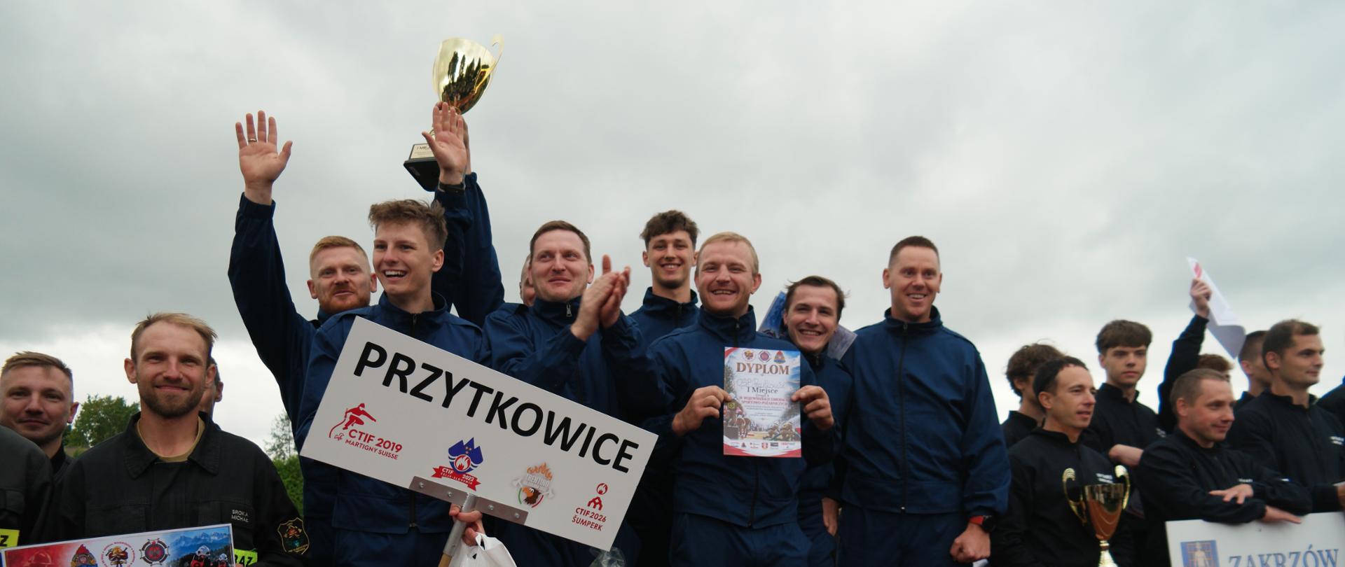 Drużyna mężczyzn z OSP Przytkowice stoi na podium z pucharem za zajęcie I miejsca.