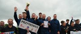 Drużyna mężczyzn z OSP Przytkowice stoi na podium z pucharem za zajęcie I miejsca.