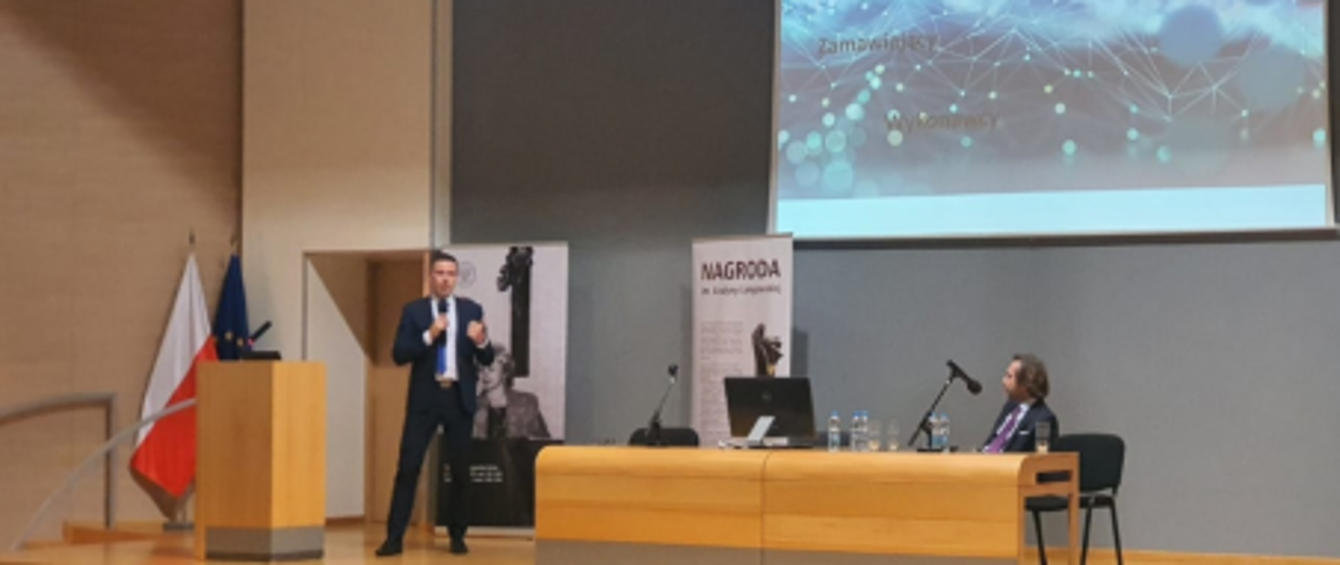 Zdjęcie z konferencji w Olsztynie. Na zdjęciu osoba prowadząca konferencję wraz z pokazem slajdów.