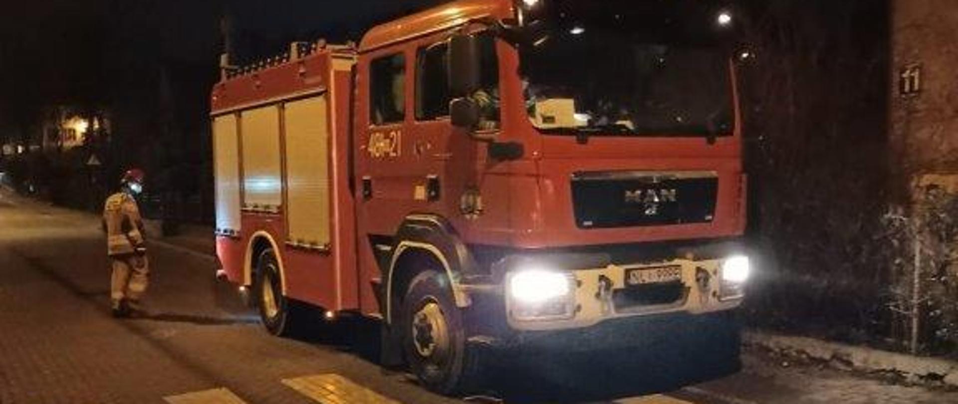 Na zdjęciu znajduję się samochód pożarniczy podczas działań. Obok niego znajduje się strażak.