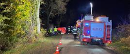 Samochody ratownicze stoją na jezdni w porze nocnej w oddali parawan i wrak pojazdu