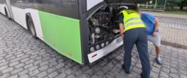 Na pierwszym planie: umundurowany funkcjonariusz zachodniopomorskiej ITD stoi z tyłu autobusu przegubowego komunikacji miejskiej i zagląda do komory silnika pojazdu. Obok inspektora stoi kierowca kontrolowanego autobusu. W tle: wiata przystankowa na jednej z pętli końcowych w Szczecinie.