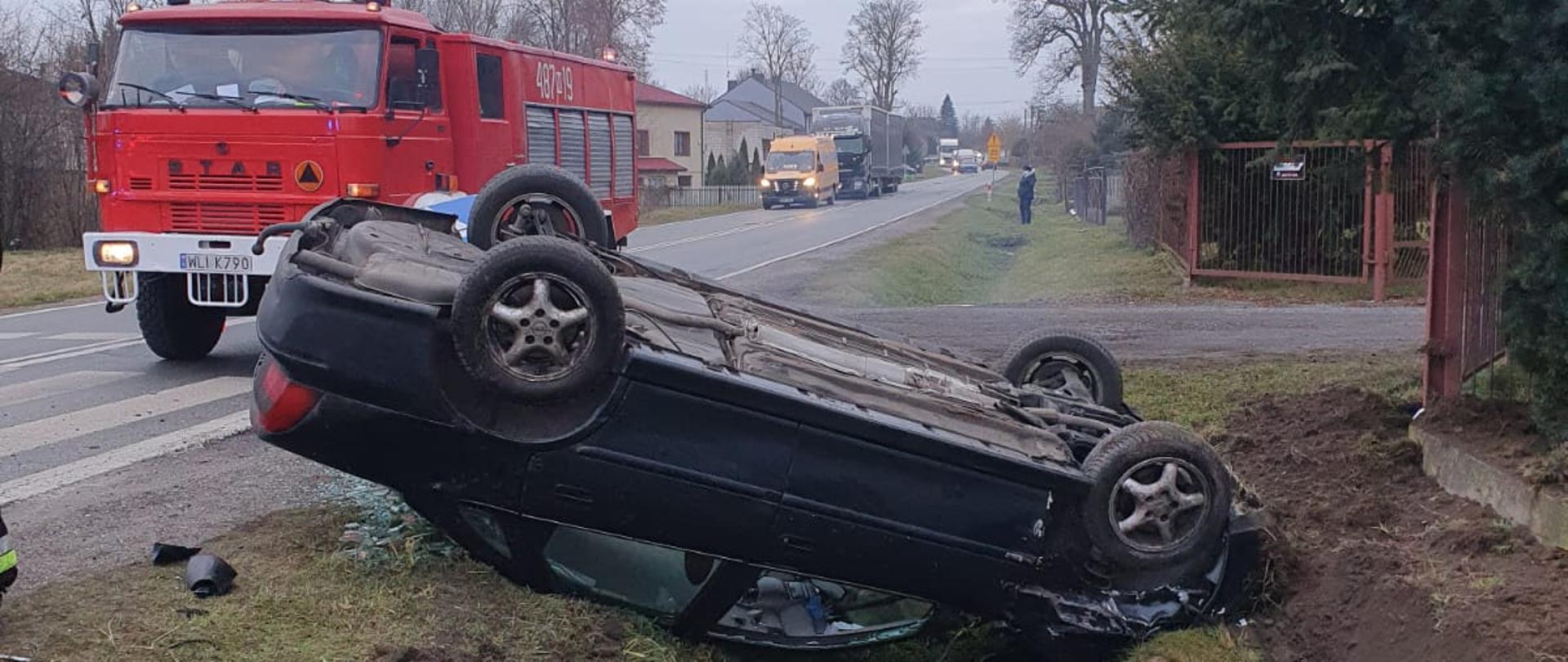wóz strażacki i samochód osobowy na dachu. Droga 747 zablokowana
