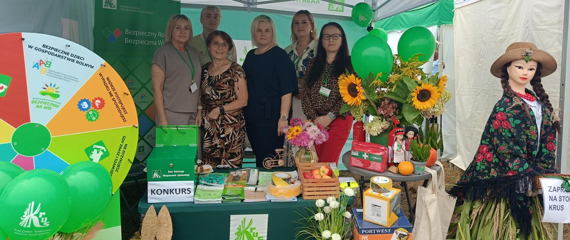 Kolorowe stoisko KRUS w biało-zielonym namiocie, pełne kolorowych dekoracji. Wewnątrz namiotu 5 pracowników oraz kierownik.
