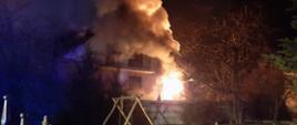 Dom dwukondygnacyjny częściowo objęty pożarem. Widoczne kłęby dymu. Pora wieczorna.