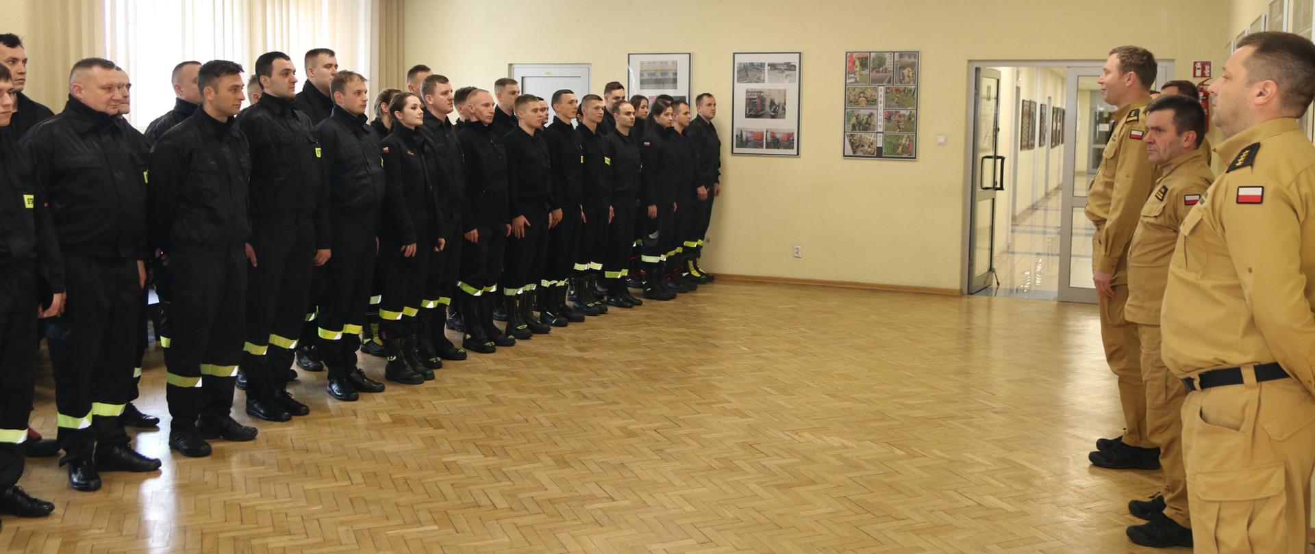 Ustawieniu w dwuszeregu słuchacze szkolenia podstawowego w czasie spotkania z kierownictwem i kadrą dydaktyczno-wychowawczą Szkoły. Słuchacze ubrani w czarne umundurowanie koszarowe, kadra w ubrania służbowe koloru musztardowego