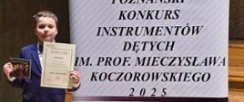 Zdjęcie przedstawia laureata Miłosza Matyszczaka stojącego na scenie z dyplomem.
