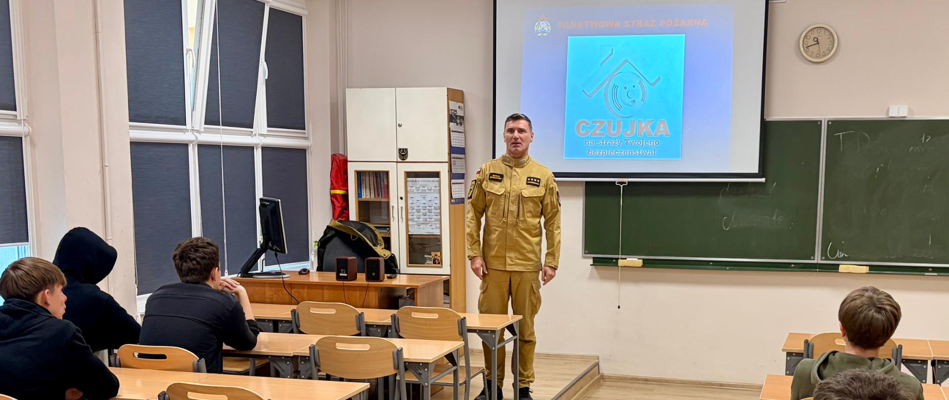 Sala lekcyjna, strażak szkoli, młodzież szkolna siedzi w ławkach
