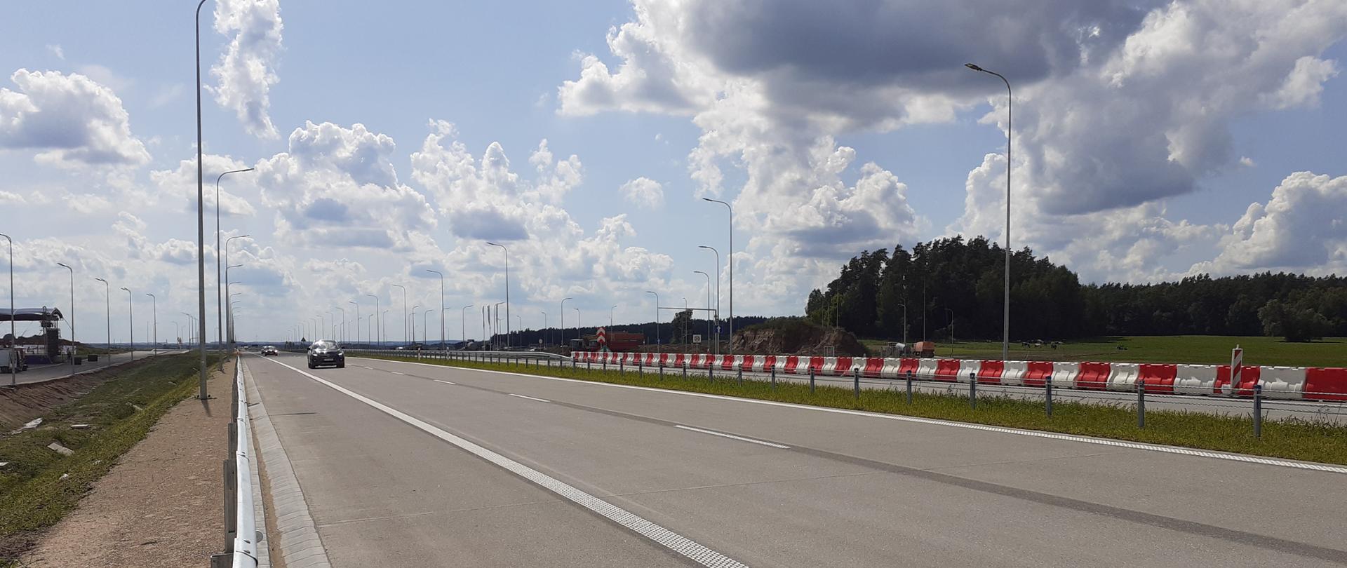 Dwujezdniowa droga ekspresowa. Nadjeżdżające samochody osobowe. Słoneczny dzień, błękitne niebo z chmurami kłębiastymi