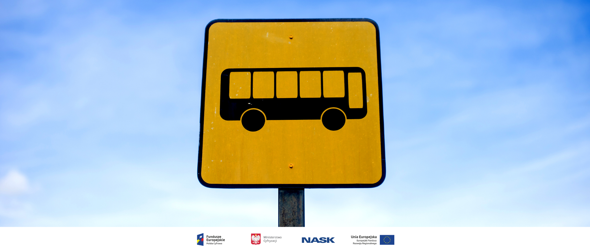 Żółty znak drogowy z autobusem. W tle błękitne niebo