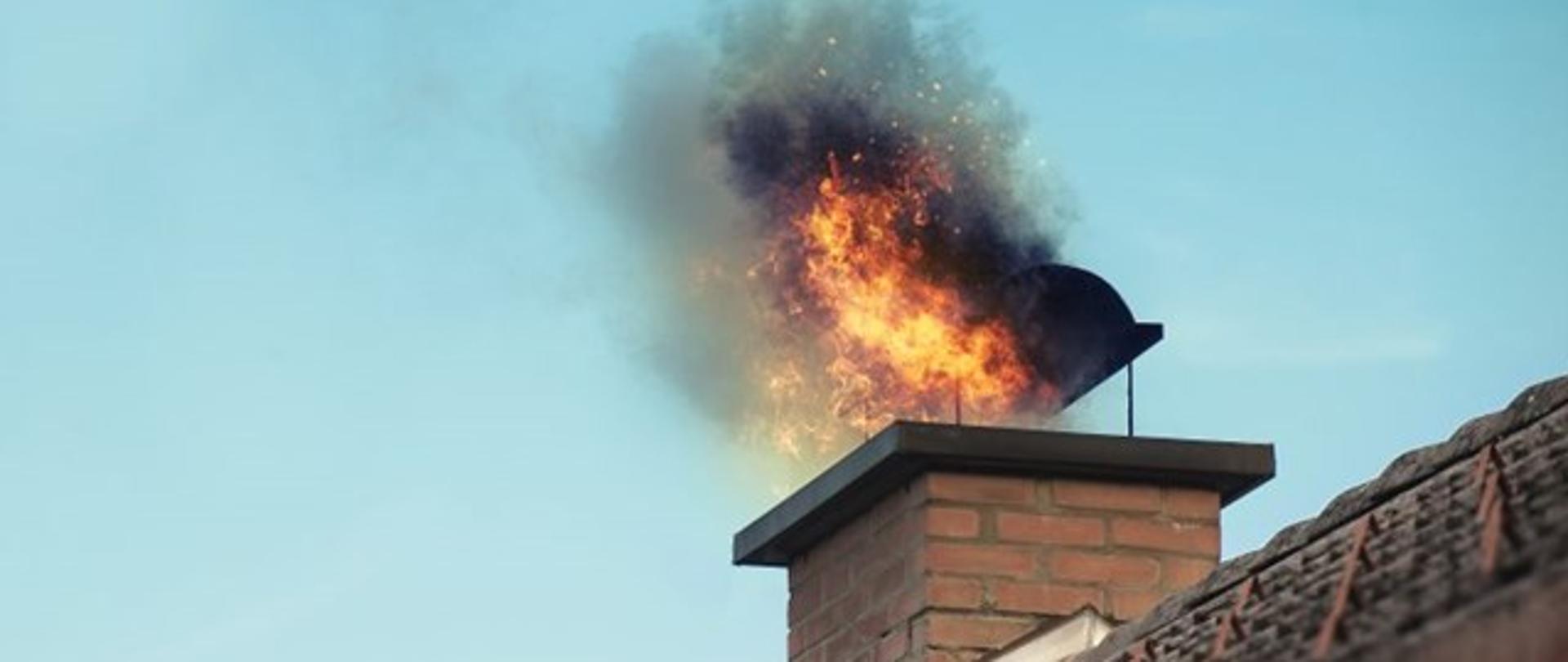 Zdjęcie przedstawia pożar sadzy w kominie. Ogień wydostaje się z komina. 