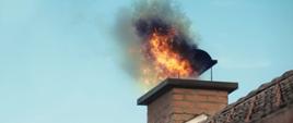 Zdjęcie przedstawia pożar sadzy w kominie. Ogień wydostaje się z komina. 