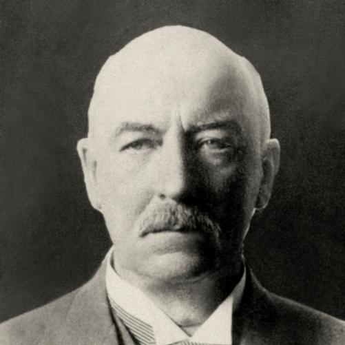 Gabriel Narutowicz - czarno-biały portret starszego łysiejącego mężczyzny, po bokach nieco siwych włosów, wąsy, ciemna marynarka, mucha w paski.