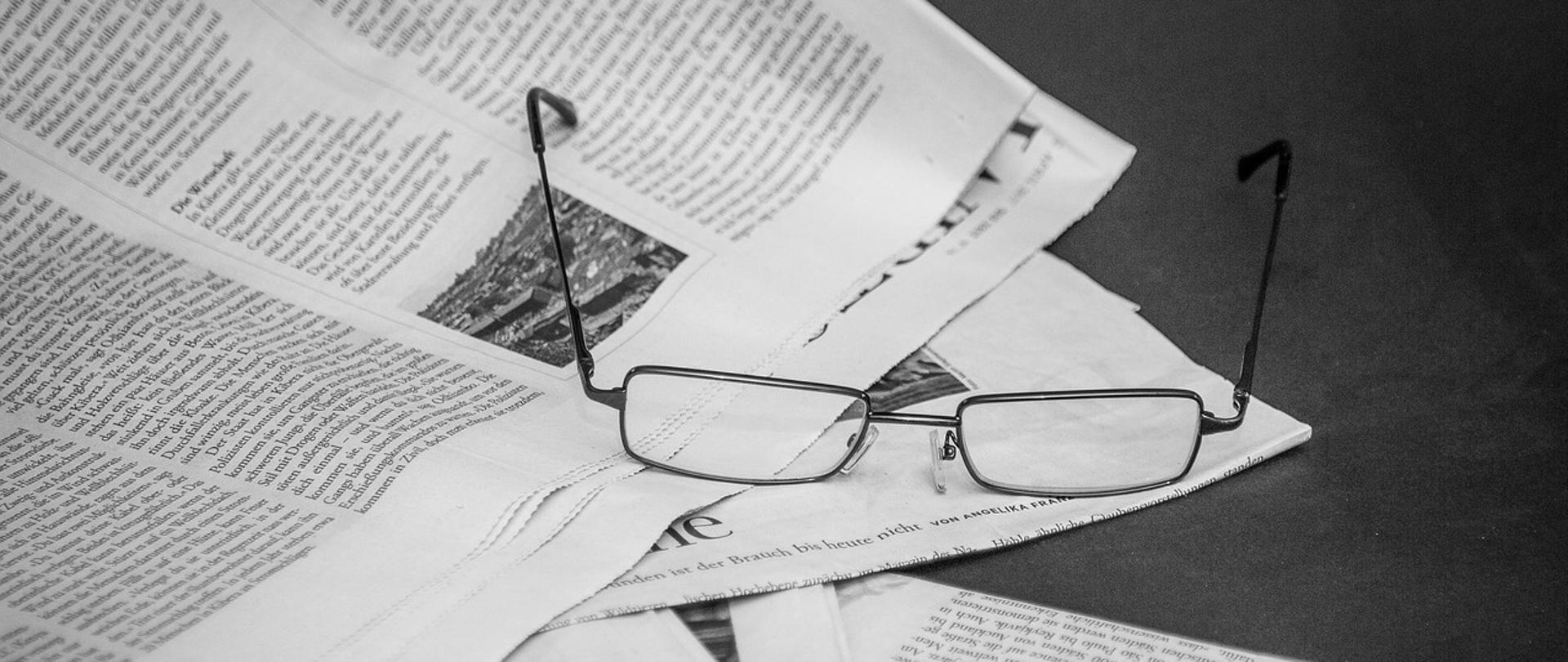 Czarno-białe zdjęcie okularów leżących na stosie gazet