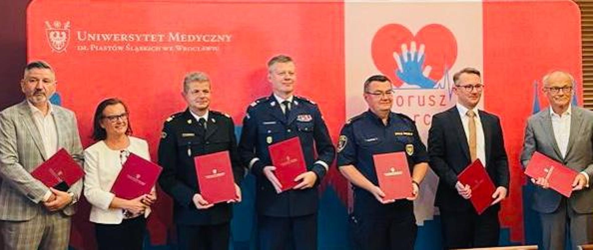 Funkcjonariusze służb mundurowych oraz osoby cywilne siedzą przy stole.