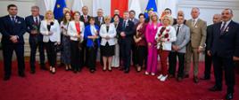 Grupa ludzi stojąca w jasnym pomieszczeniu na czerwonym dywanie
