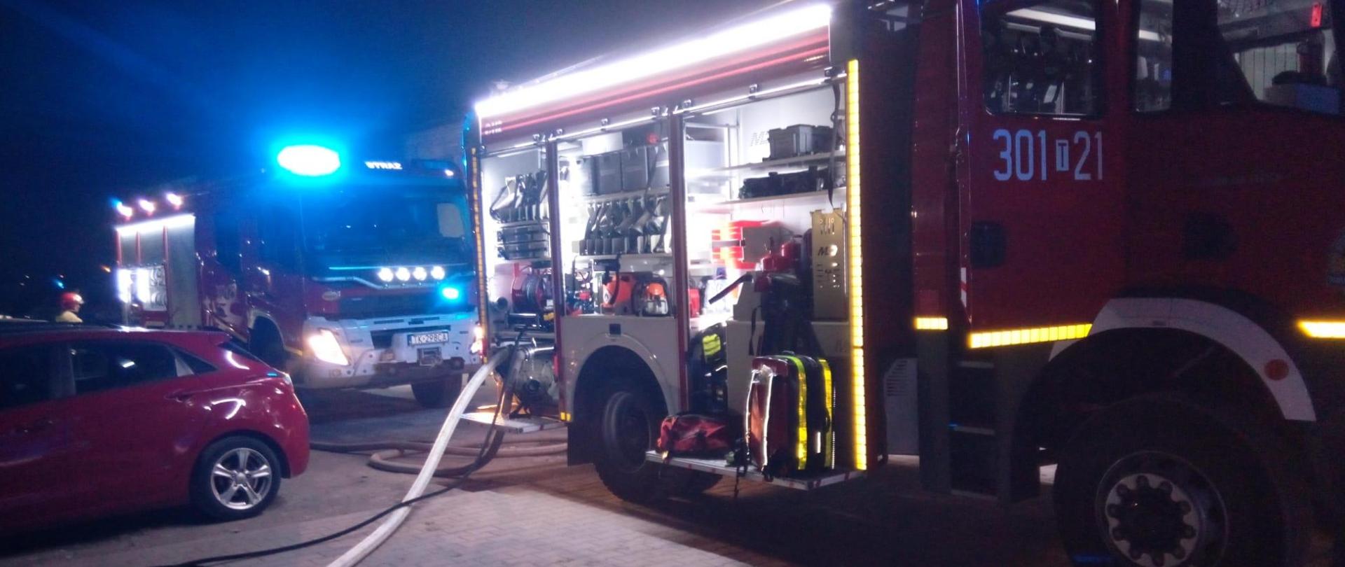 Zdjęcie przedstawia dwa samochody gaśnicze, które przybyły na pomoc. Wąż gaśniczy podpięty do pierwszego z nich rozciągnięty jest na ziemi, przy nim leży wąż szybkiego natarcia.