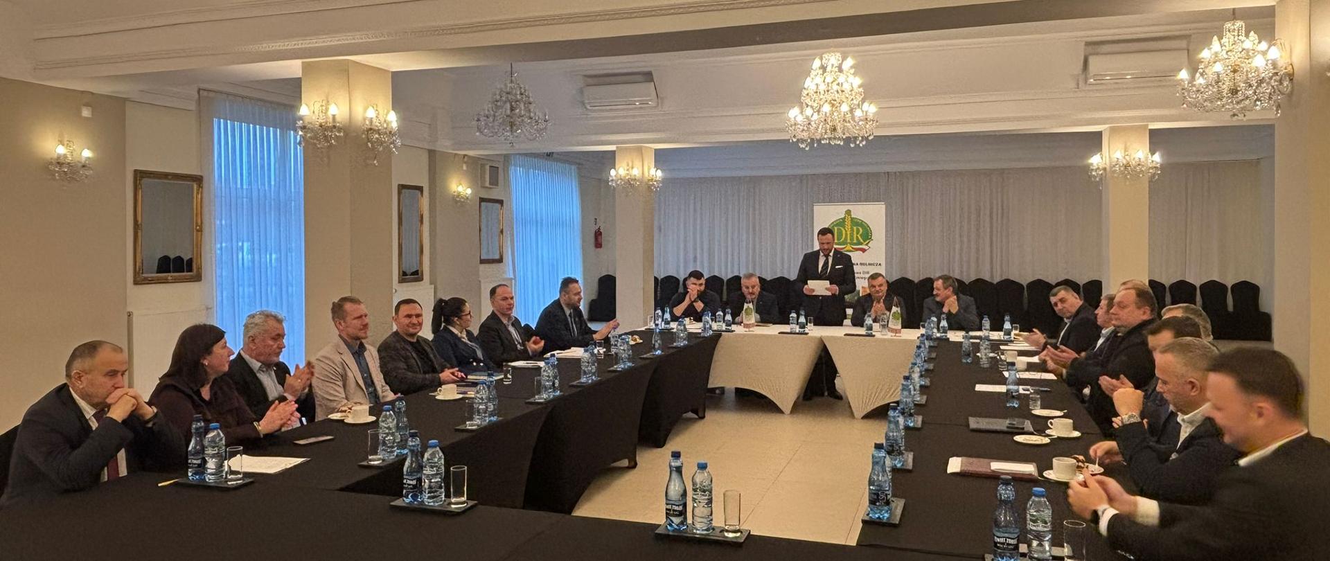 Uczestnicy Posiedzenia siedzący na sali konferencyjnej wraz z osobą przemawiającą.