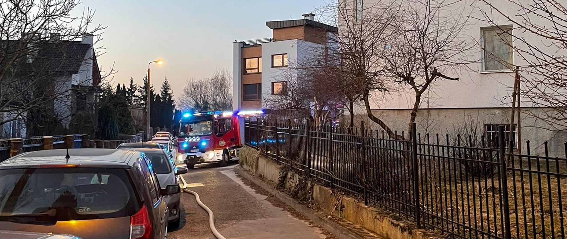 Niewielki budynek gospodarczy około 2 na 2 metry. Widoczne tylko dwie ściany z otworami po oknach i drzwiach. Budynek wypełniony dymem a w środku widać jeszcze ogień