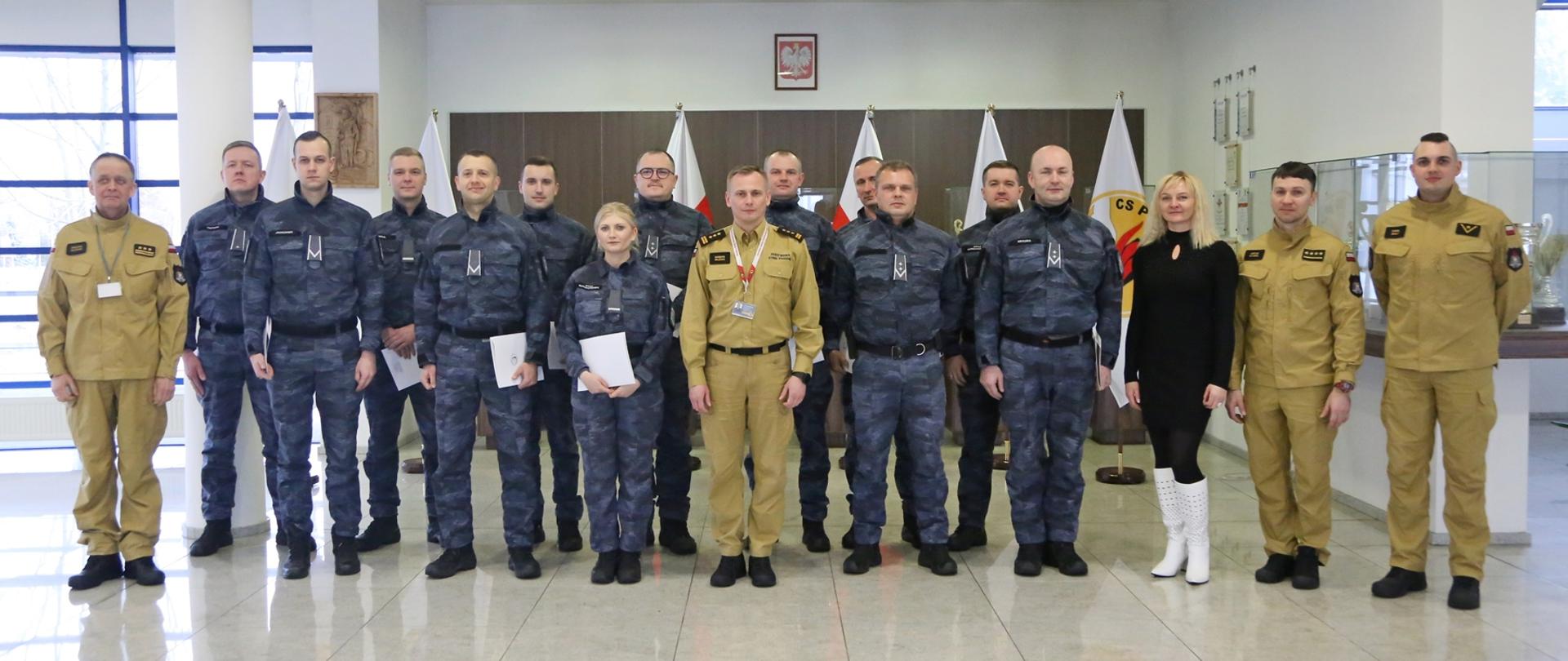 Grupowe zdjęcie uczestników szkolenia (12 osób) w towarzystwie Zastępcy Komendanta Centralnej Szkoły PSP, kobiety oraz trzech strażaków CS PSP