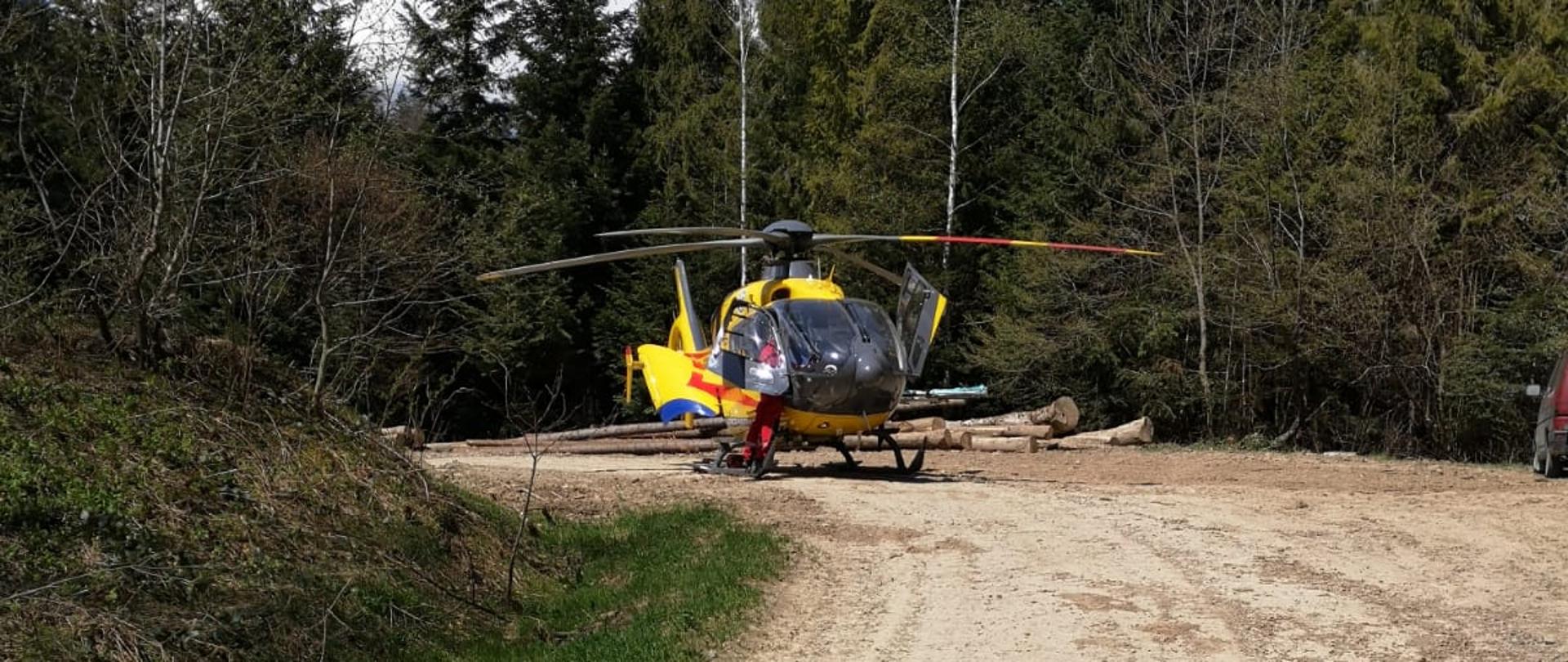 Na zdjęciu widać śmigłowiec Lotniczego Pogotowia Ratunkowego który przygotowuje się do startu na drodze szutrowej. W około las.