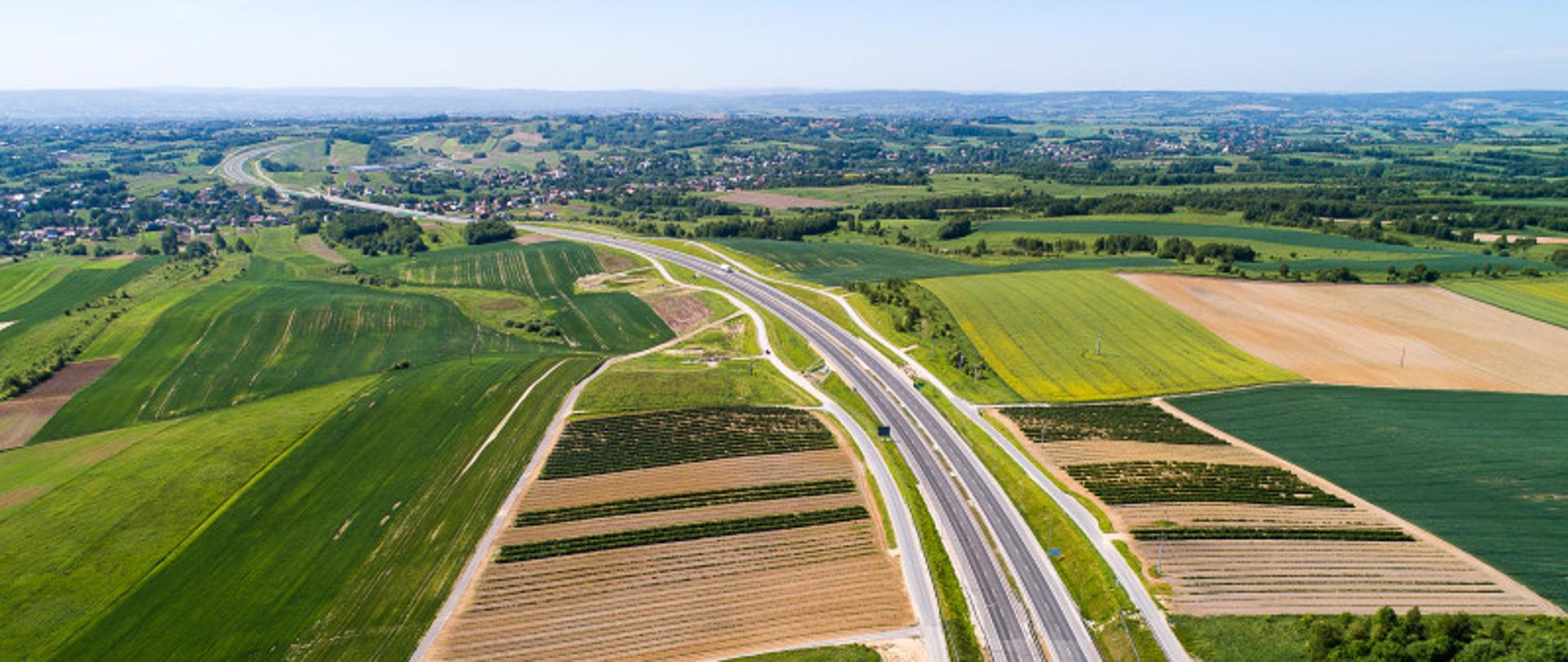 Widok z góry na dwujezdniową drogę biegnącą wśród pól i łąk 
