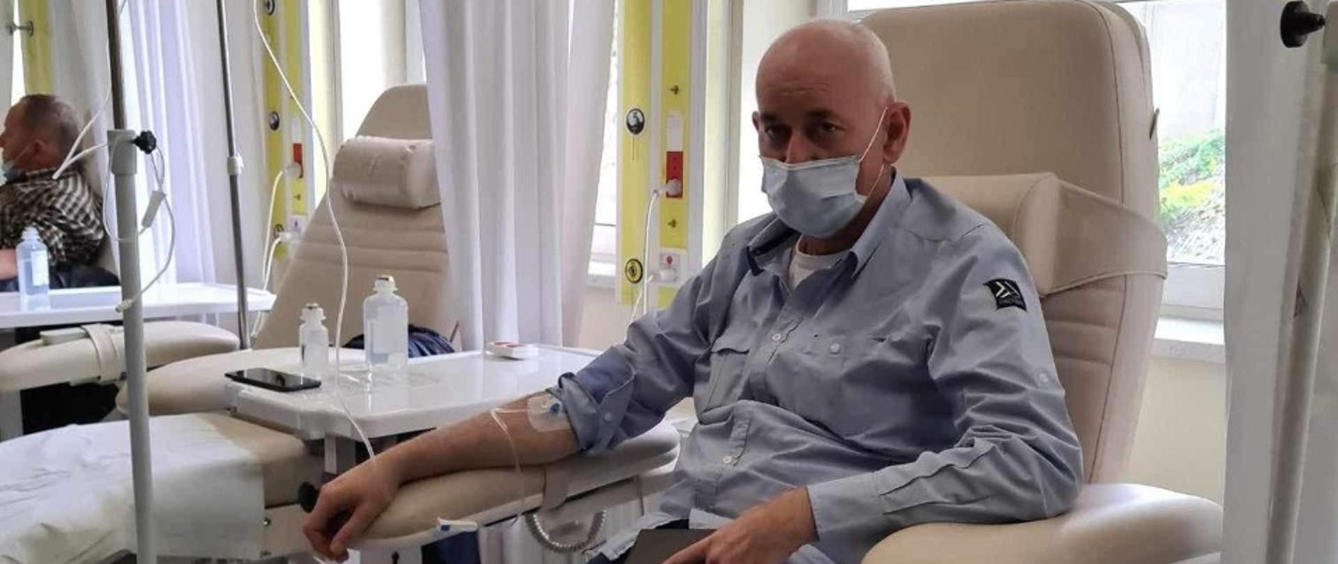 Mężczyzna potrzebujący pomocy siedzi na fotelu przyjmując kroplówkę