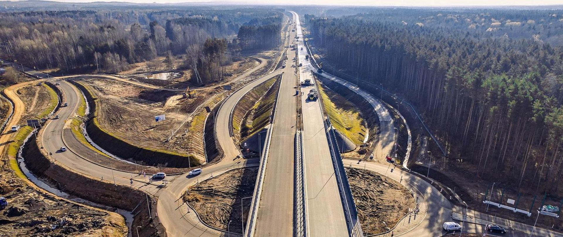 Widok z lotu ptaka na prace prowadzone na drodze krajowej nr 78. Wokół budowanej trasy widoczny las.
