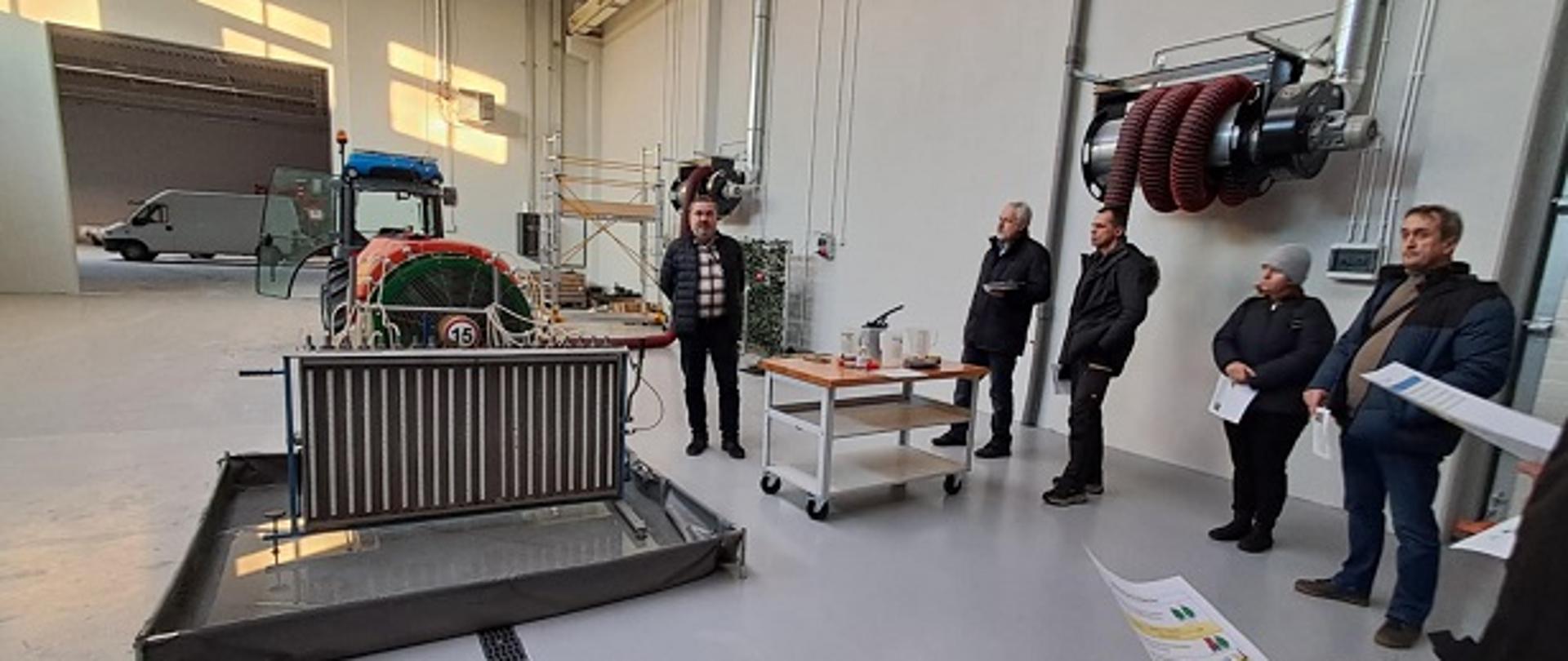 Wykładowca stojący obok opryskiwacza i sprzętu przeznaczonego do jego badania. 