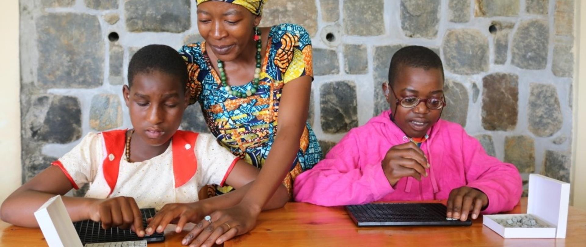 dwóch chłopców wraz z nauczycielką układa klocki służące do nauki matematyki