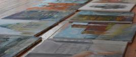 Na zdjęciu rozłożone na drewnianej podłodze prace malarskie uczniów łódzkiego Plastyka