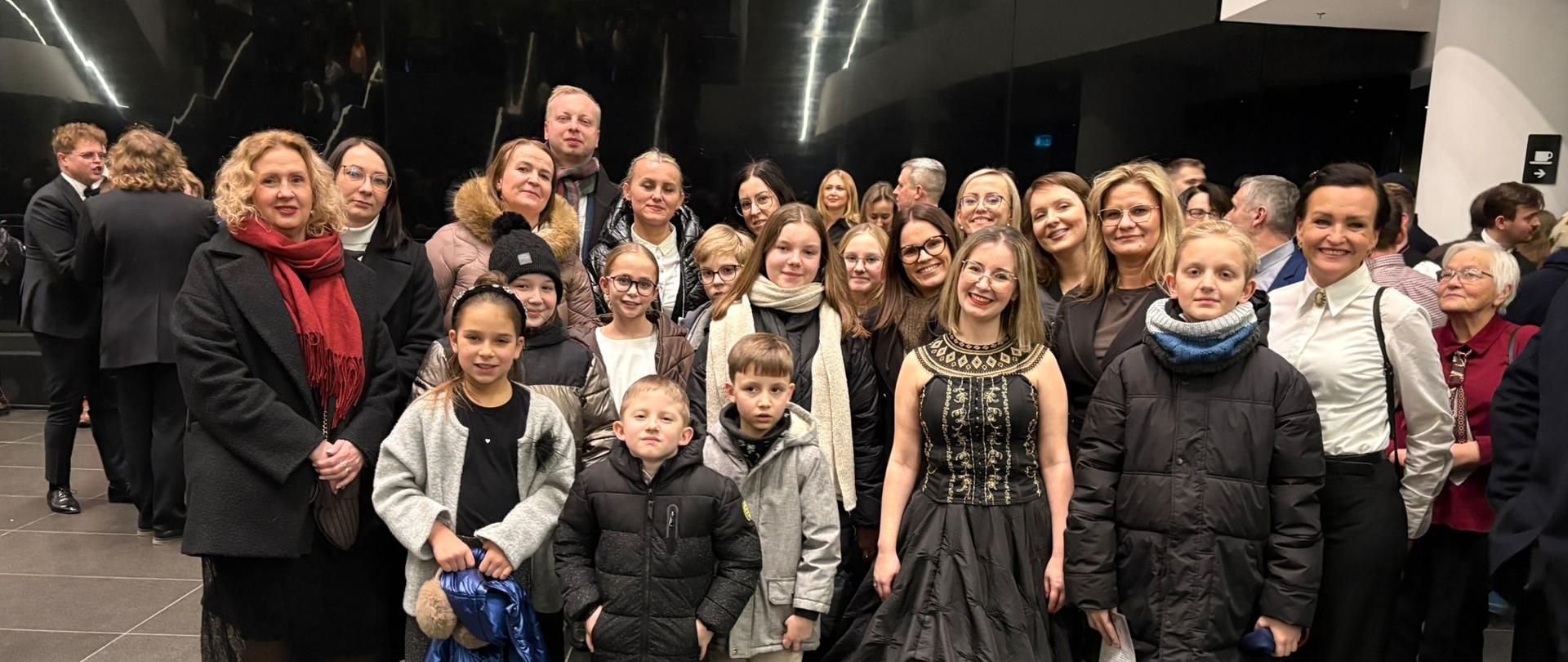 Grupa osób w holu Narodowego Forum Muzyki we Wrocławiu.