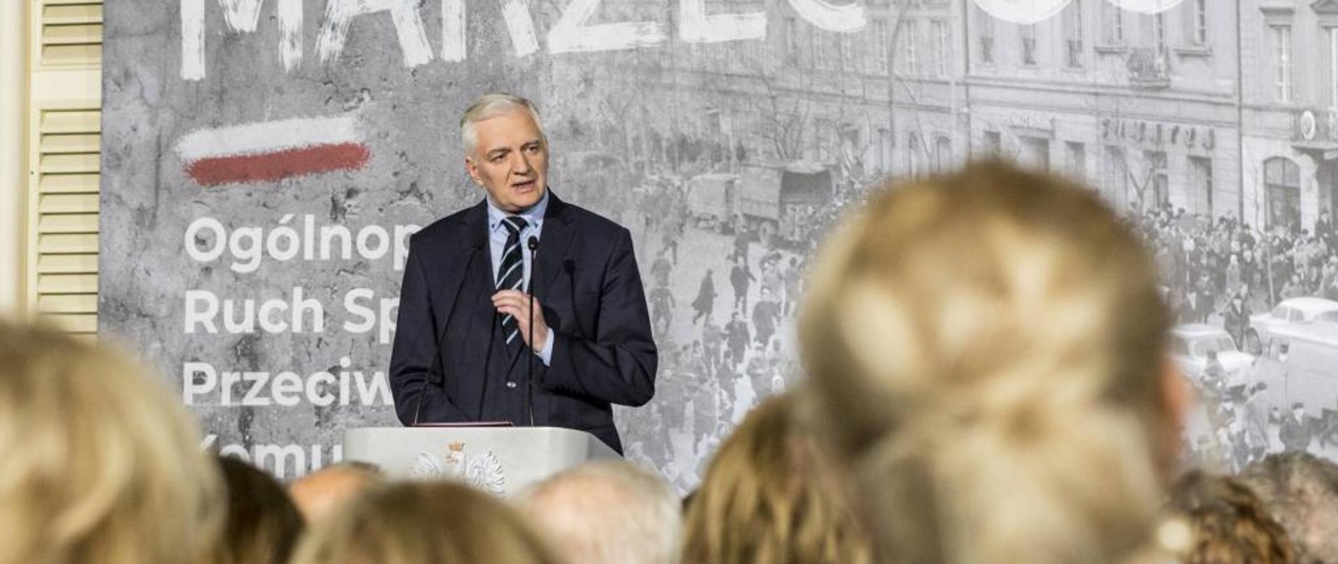 Jarosław Gowin przemawia do mikrofonu, w tle napis Marzec'68