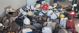 Zdjęcie przedstawia sprzęt strażacki: węże, buty, hełmy, urania znajdujące się na posadzce w garażu, które będą przekazane strażakom z Ukrainy, 