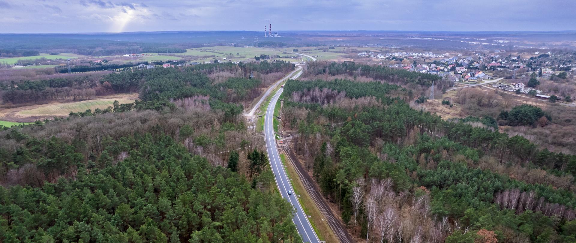 Widok z góry na jednojezdniową drogę biegnącą przez las, pochmurne niebo
