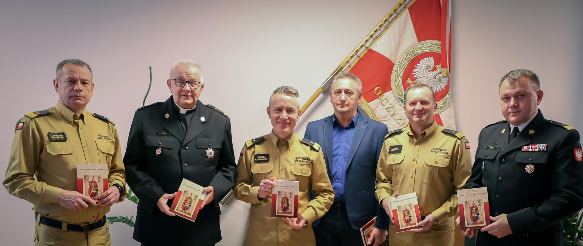 sześciu strażaków, którzy prezentują w dłoniach książkę "Etos Rycerzy św. Floriana"