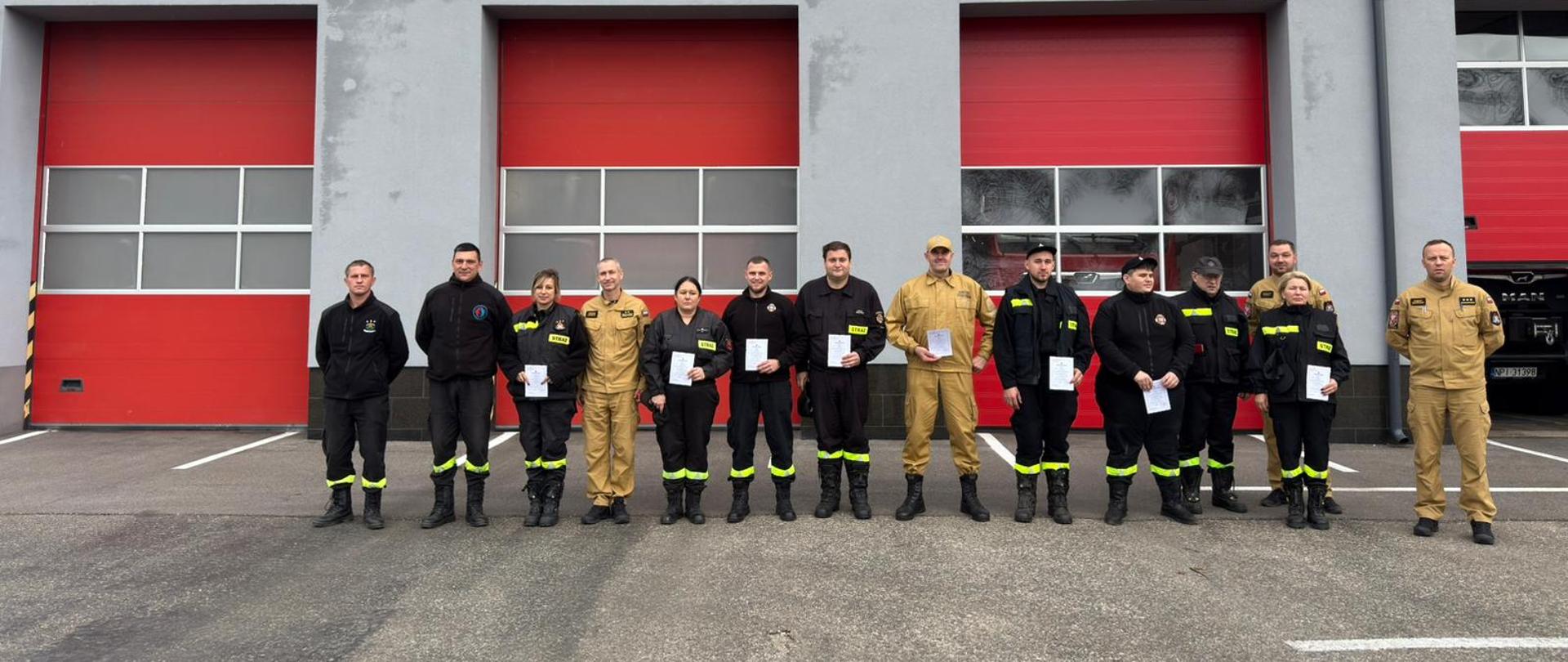 Strażacy OSP oraz PSP na tle strażnicy, stojący po zdanym kursie.
