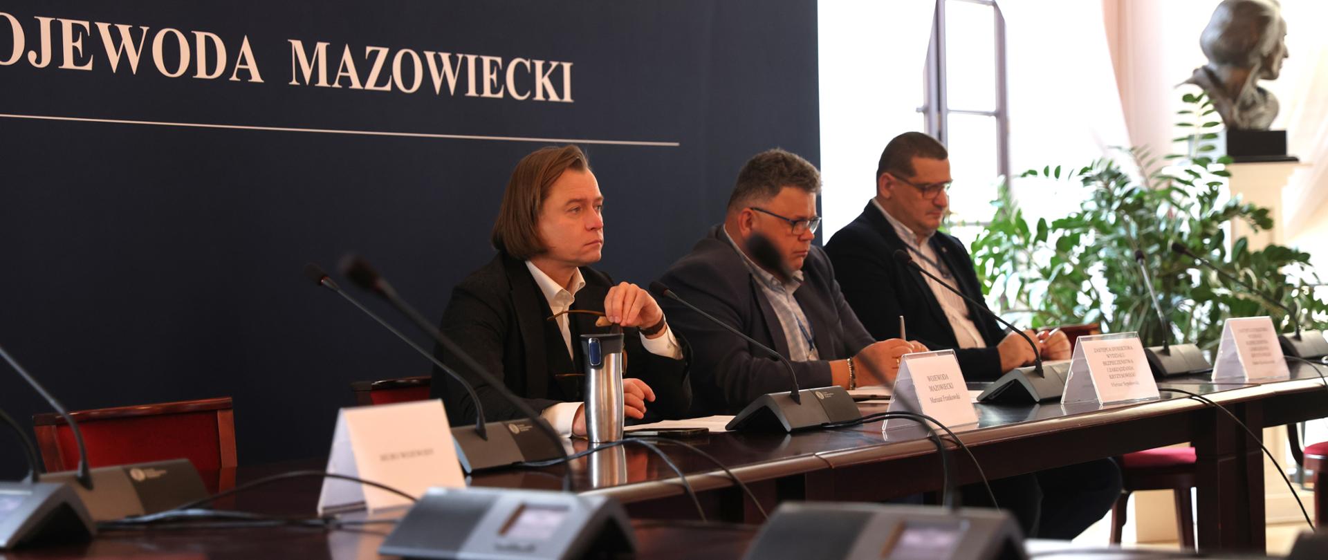 Na zdjęciu z lewej strony Wojewoda Mazowiecki siedzi przy stole, po prawej są dyrektorzy Wydziału Bezpieczeństwa i Zarządzania Kryzysowego.