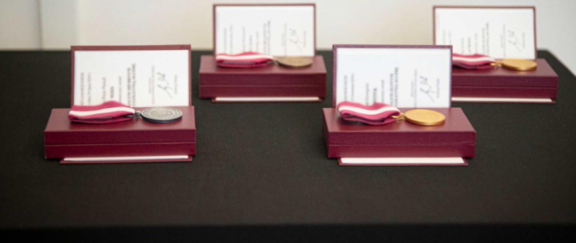 Zbliżenie na cztery medale w etui z certyfikatami, ułożone na czarnej powierzchni.
