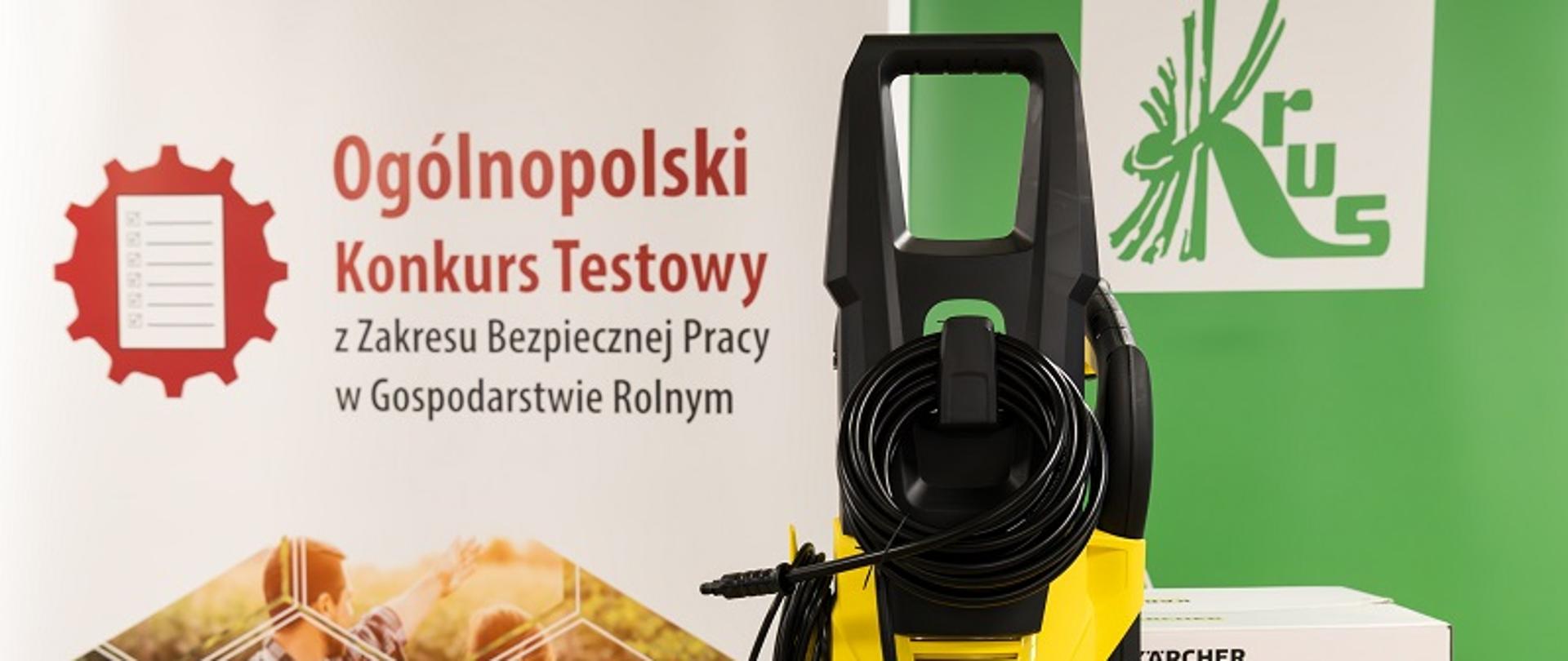 Myjka wysokociśnieniowa na tle plakatu Ogólnopolskiego Konkursu Testowego z Zakresu Bezpieczeństwa w Gospodarstwie Rolnym